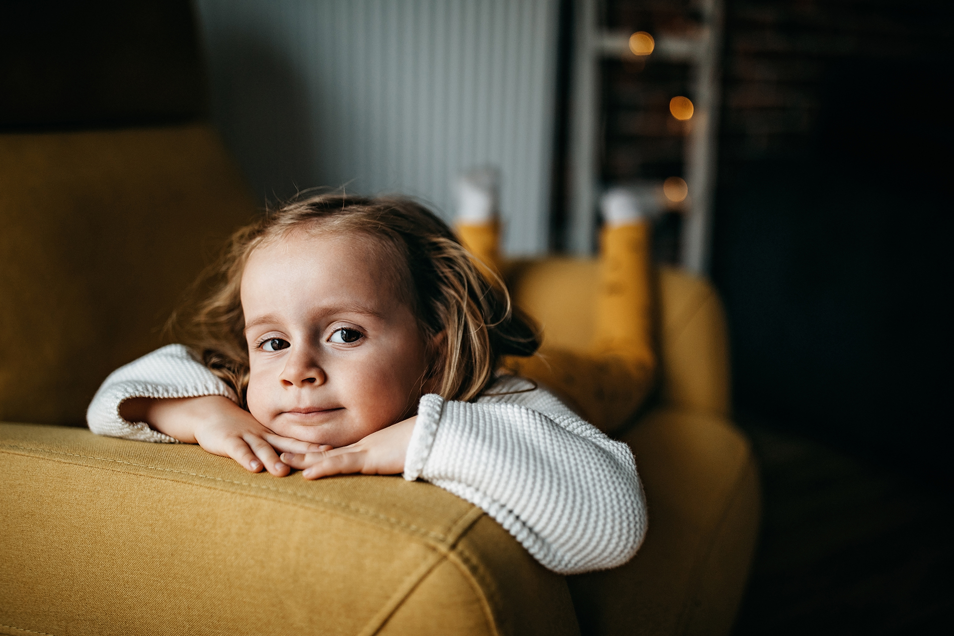 Lapsi kärsii päänsärystä ja nojaa sohvan käsinojaa vasten.