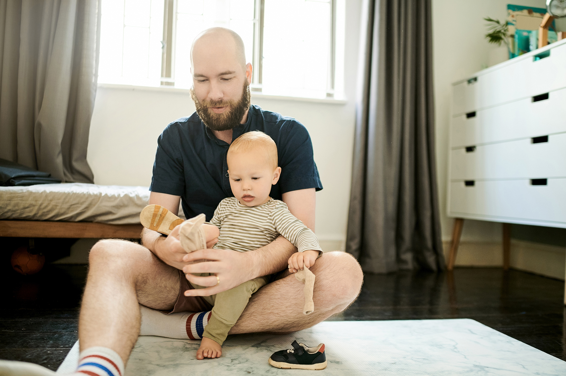 Maitoallergiasta kärsivä lapsi istuu isän sylissä, joka laittaa lapselle sukkia jalkaan.